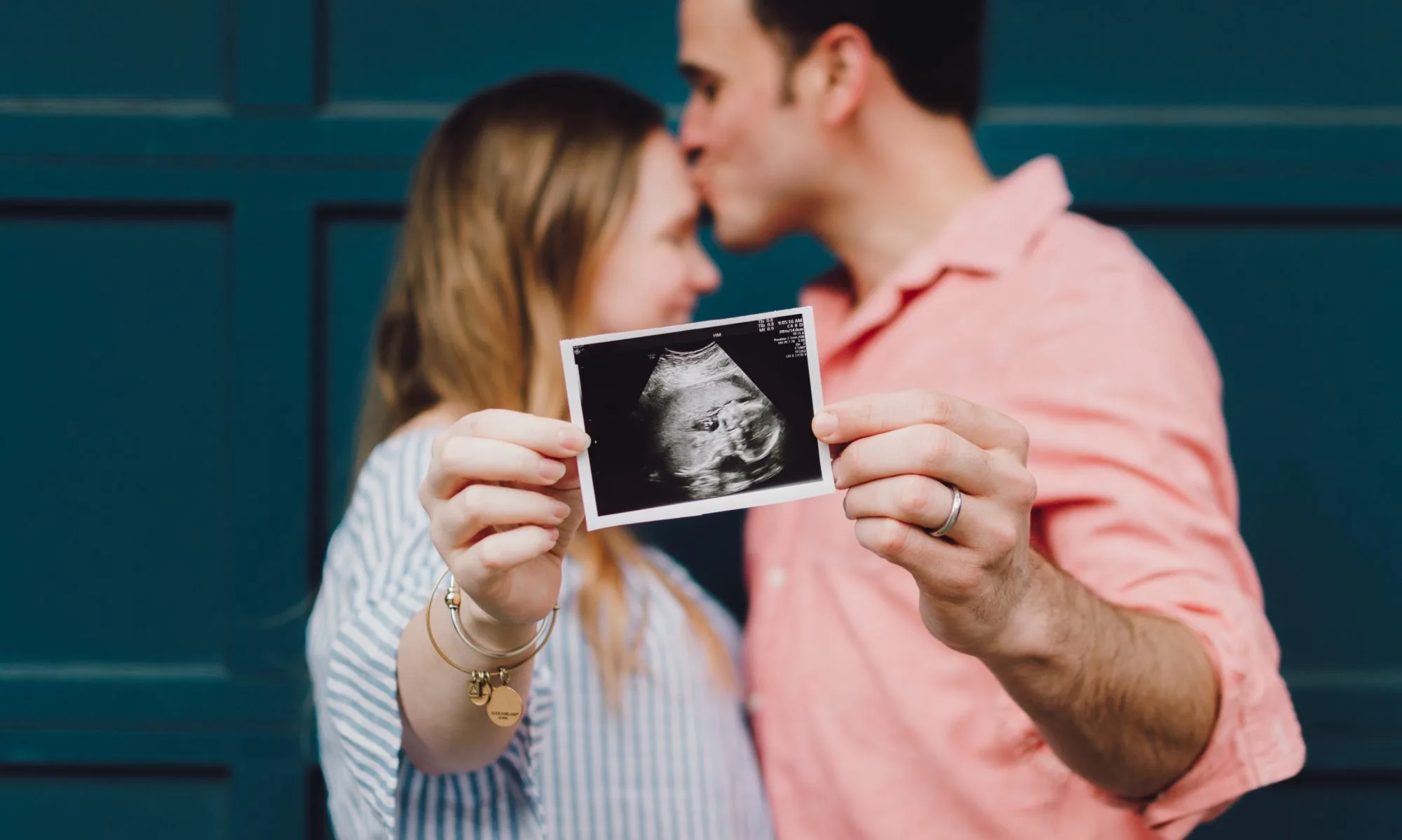 A loving couple kissing, with an ultrasound photo of their unborn child, capturing a moment of joy and anticipation.